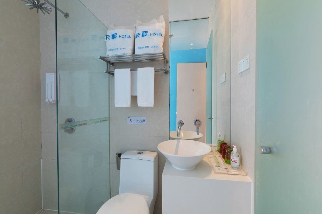 A modern bathroom with a glass shower enclosure, a white sink, and a toilet. There are two white towels hanging on a shelf above the sink.