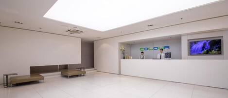 A modern reception area with a flat-screen TV, a reception desk, and a seating area with benches.