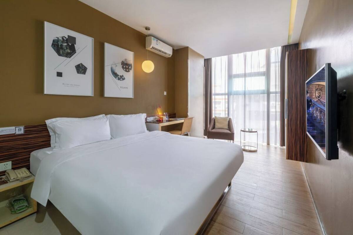 A hotel room with a large bed, a desk, a chair, and a TV.