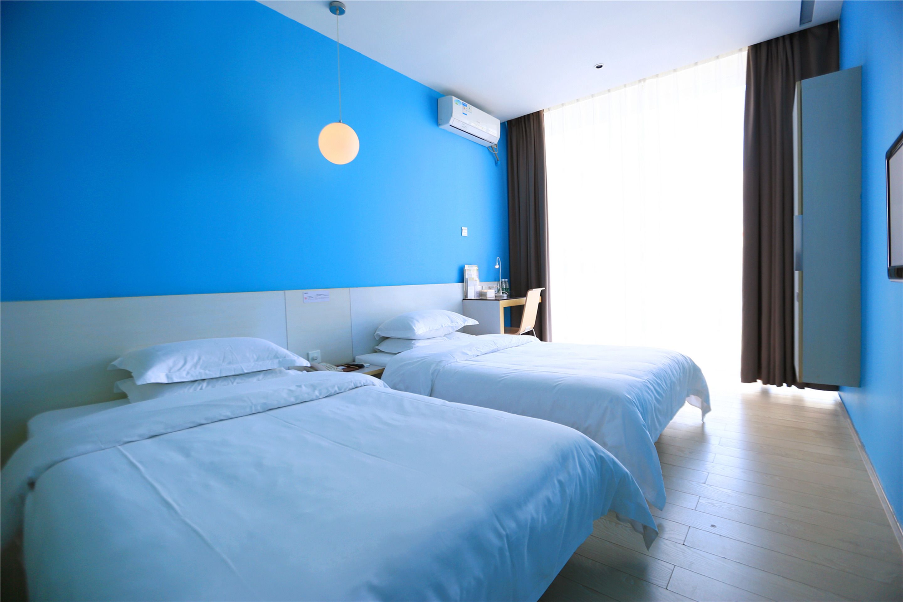 Une chambre d’hôtel avec deux lits, un bureau et une grande fenêtre avec des rideaux.