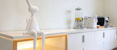 A modern kitchen with a white countertop, a coffee machine, a coffee maker, and a unique white sculpture.