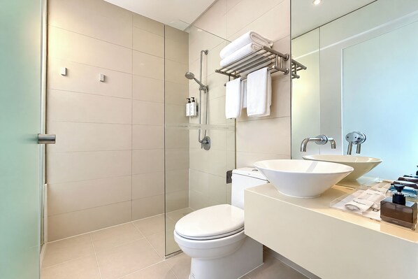 Un baño moderno con cabina de ducha de vidrio, inodoro blanco y tocador con lavabo grande y espejo.