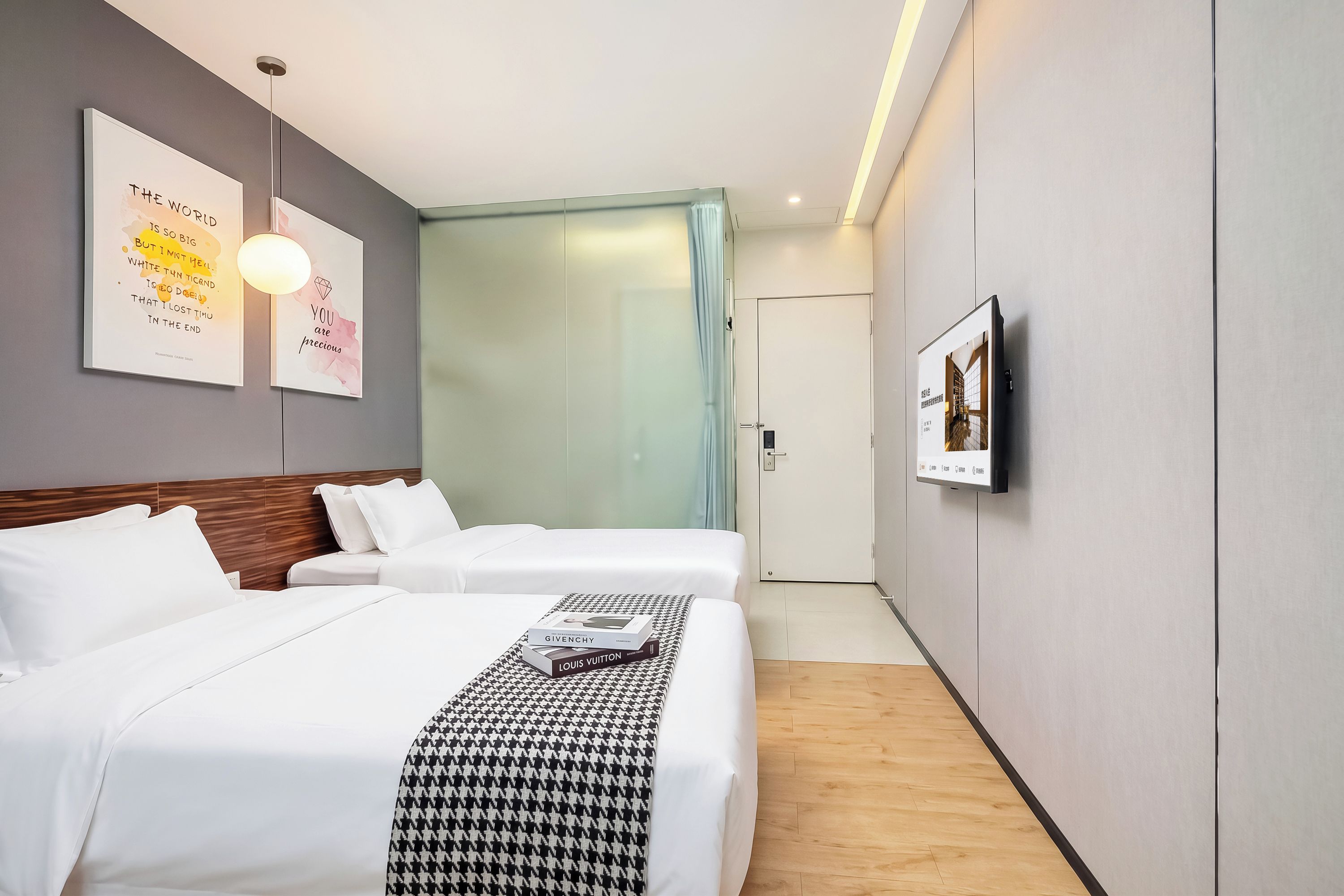 Una habitación de hotel con dos camas, un televisor montado en la pared y una cita enmarcada.