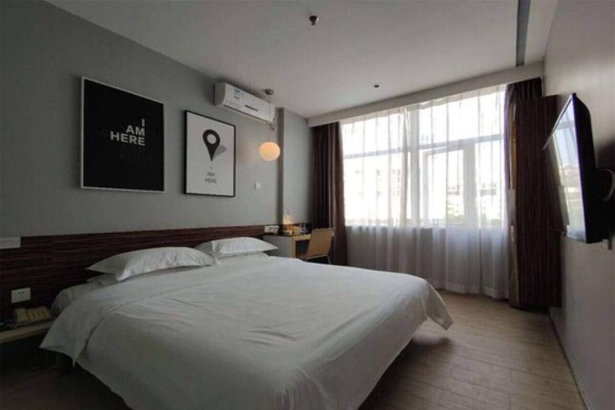 A hotel room with a large bed, a flat-screen TV, a desk with a lamp, and a window with curtains.