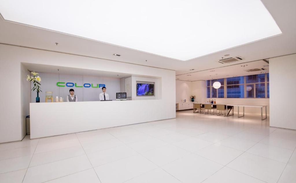 Una moderna zona de recepción con un mostrador blanco identificado con 'COLOUR' y una pantalla de televisión sobre él.