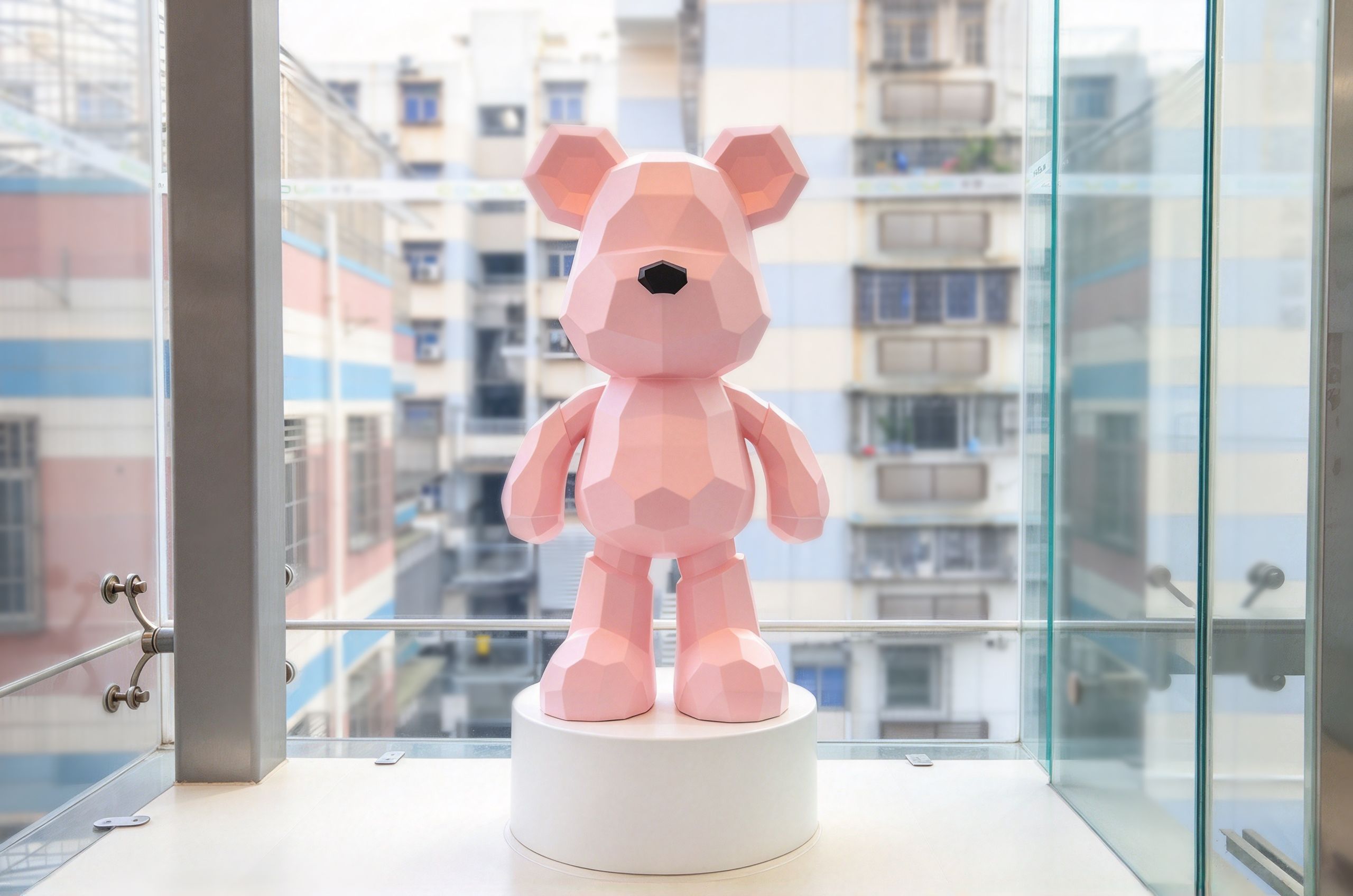 A geometric bear sculpture on a pedestal in a modern building with a view of other buildings.