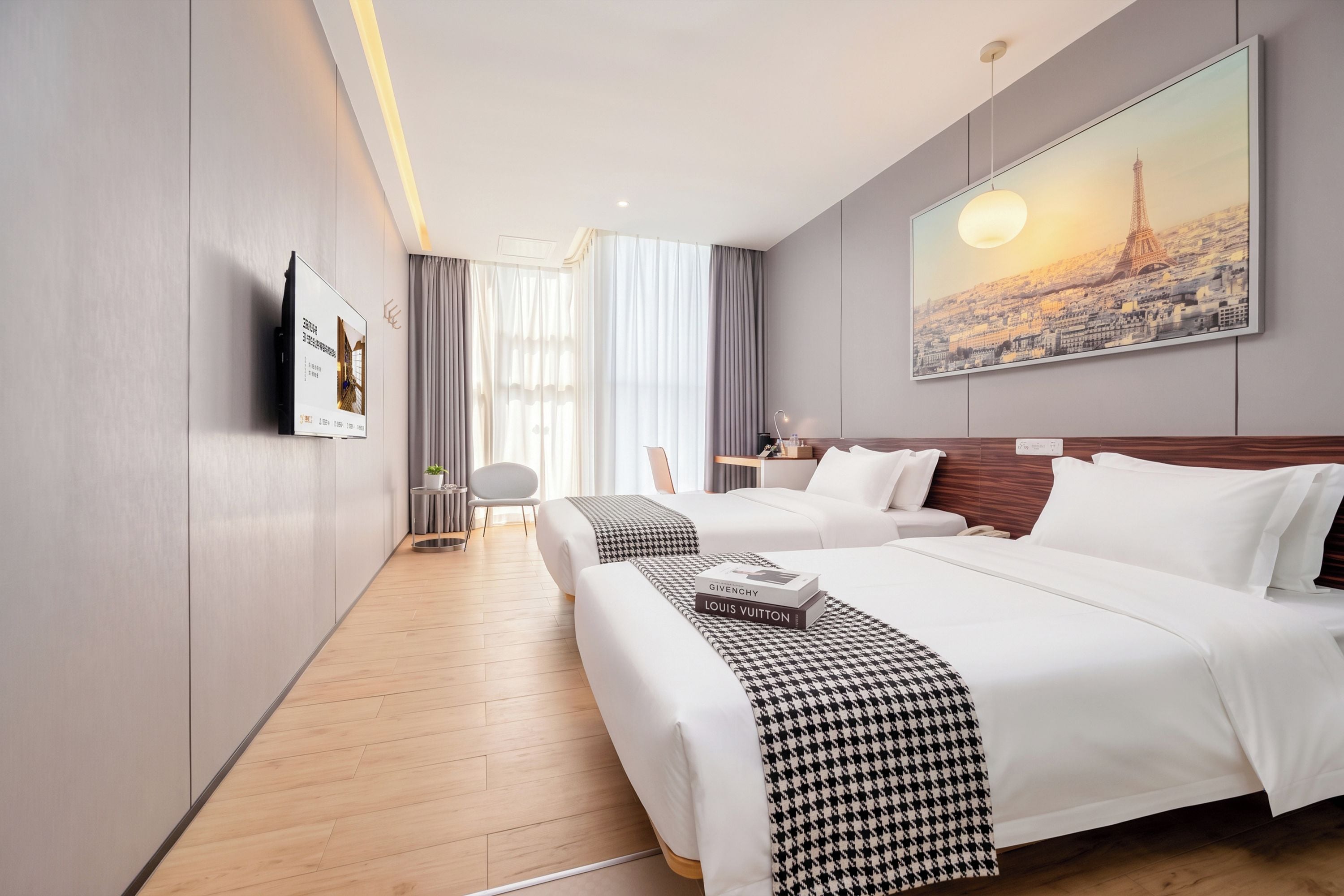 A hotel room with two beds, a large painting of the Eiffel Tower, a flat-screen TV, and a wooden floor.