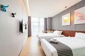 Hotellihuone, jossa on kaksi sänkyä, puulattia, yöpöytä, lamppu ja seinälle asennettu televisio.