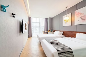 Habitación de hotel con dos camas, piso de madera, mesita de noche, lámpara y televisor montado en la pared.