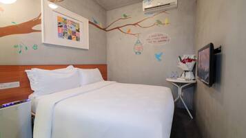 A hotel room with a bed, a small table with a vase of flowers, an air conditioner, and wall decorations including a framed picture and bird illustrations.