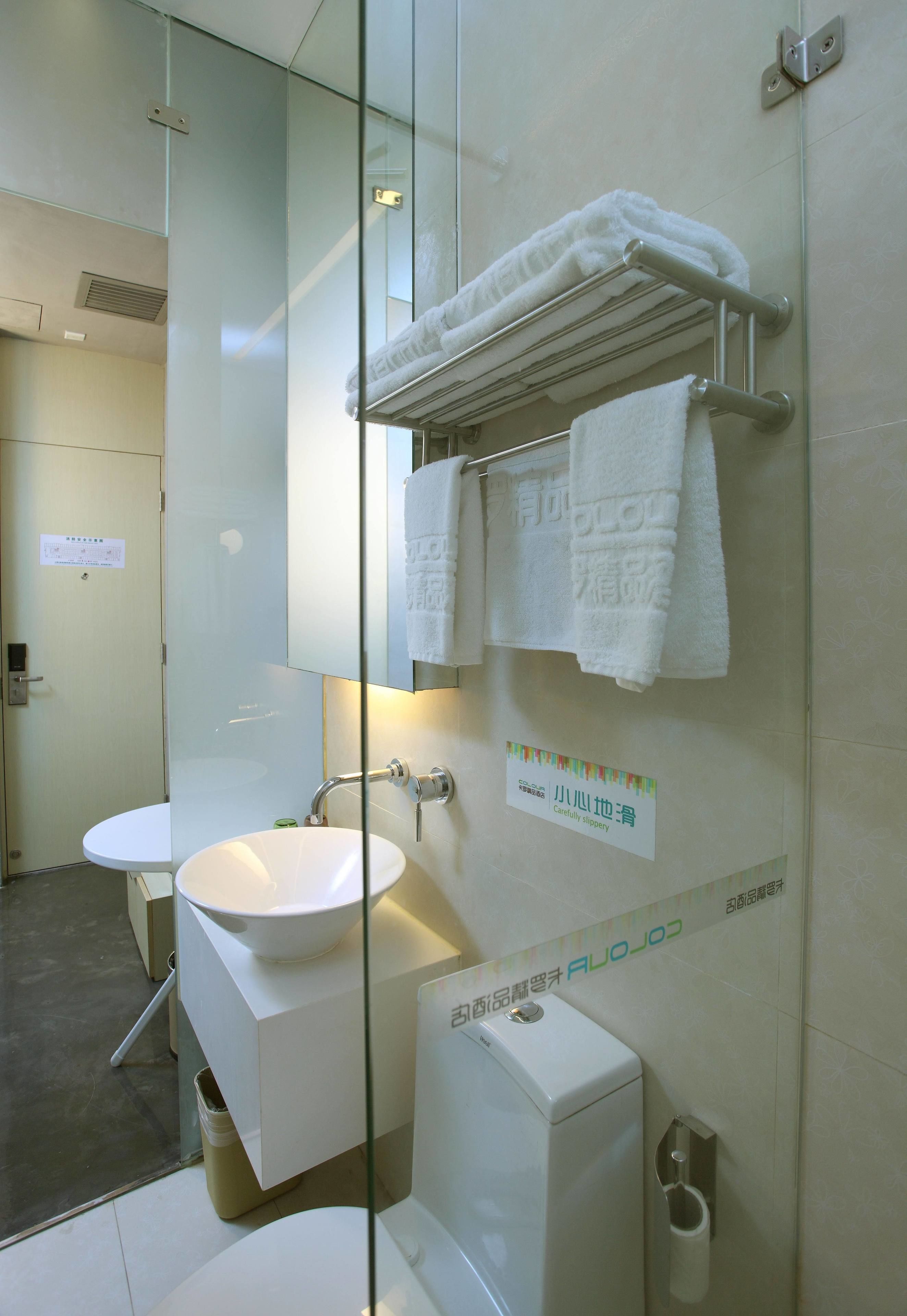 A modern bathroom with a glass partition, a white sink, a toilet, and a towel rack.