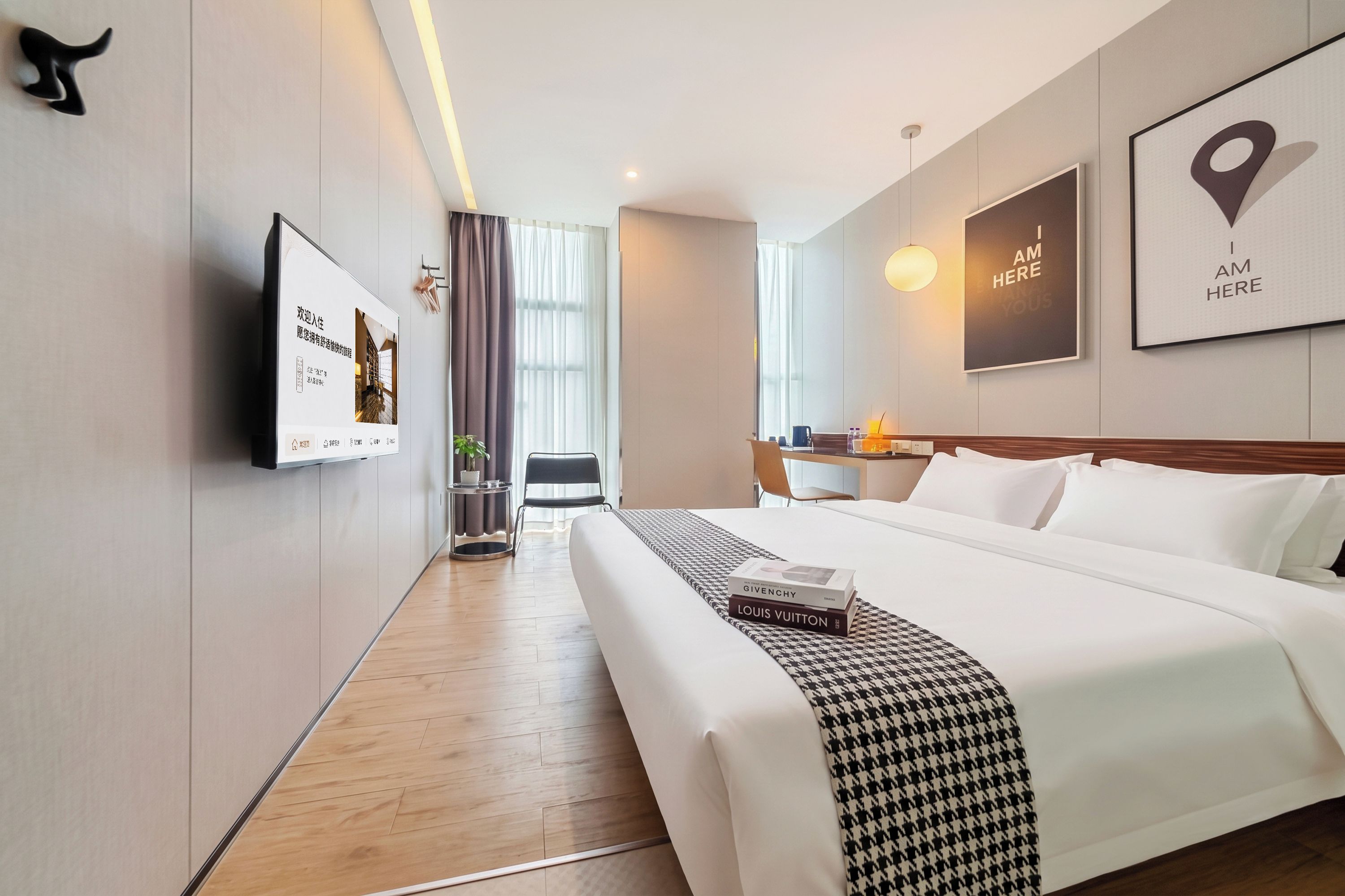 Quarto de hotel com cama, escrivaninha, cadeira, planta em vaso e vista para o corredor.