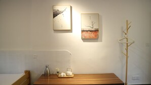 A room with a wooden bed, a table with a tray of tea items, and two framed artworks on the wall.
