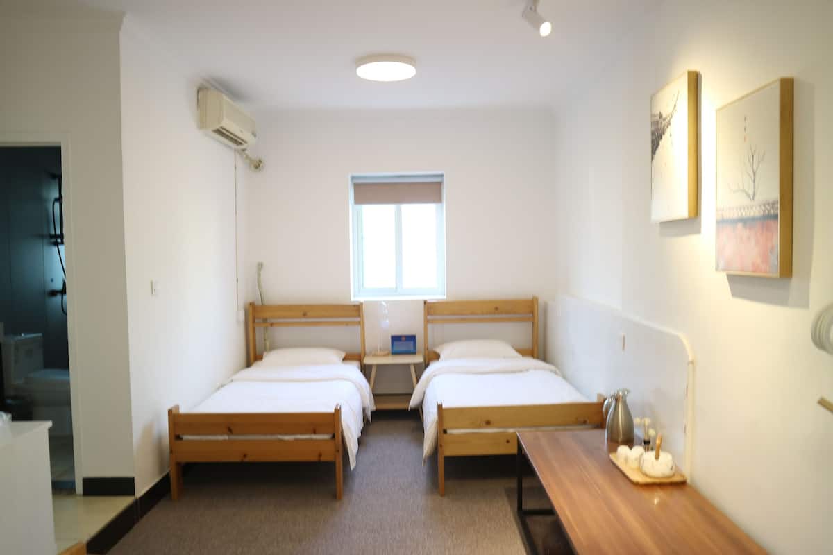 Un dormitorio doble con dos camas, una mesita de noche, una ventana y aire acondicionado instalado en la pared.