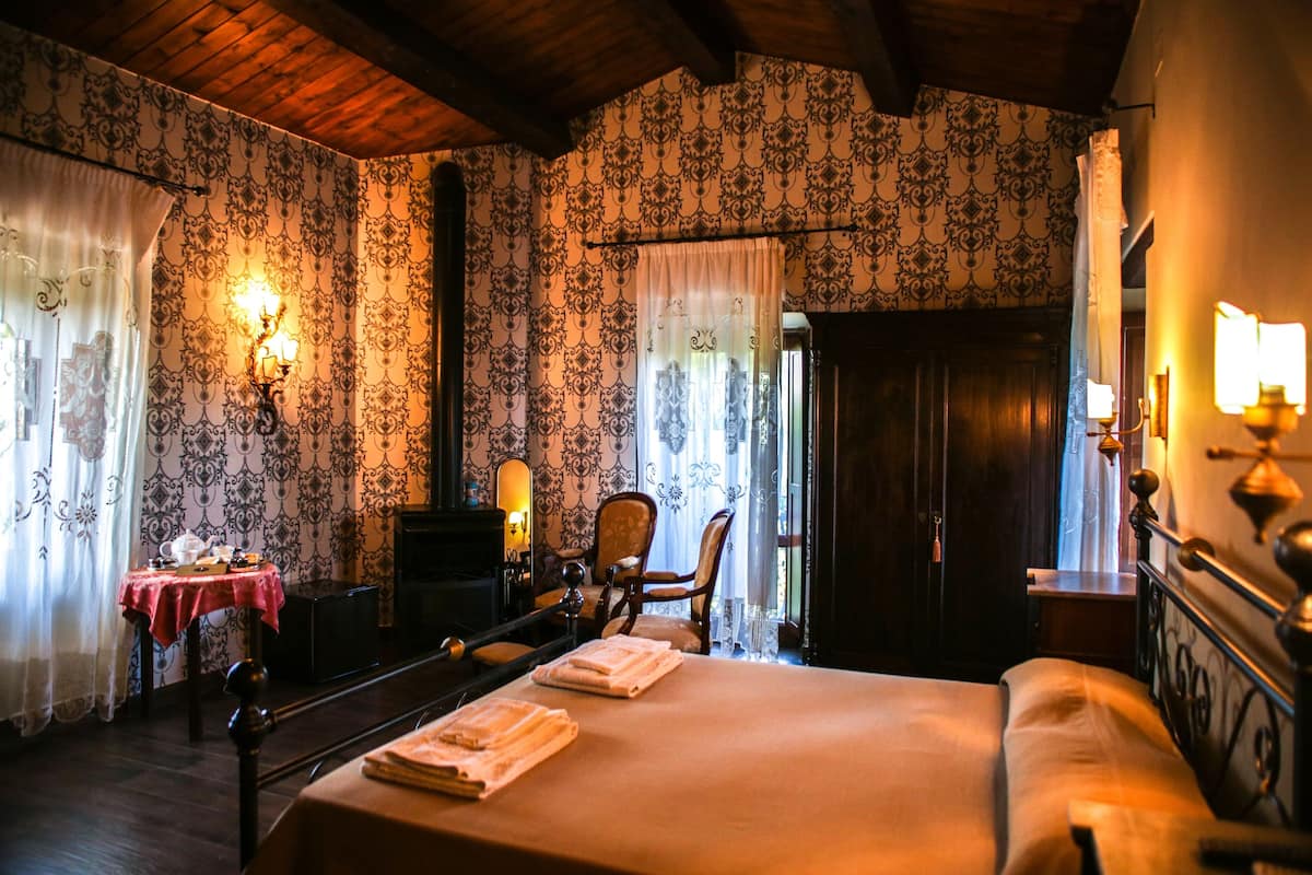 Une chambre avec un grand lit, un bureau avec une chaise, une table recouverte d’une nappe rouge et un miroir.