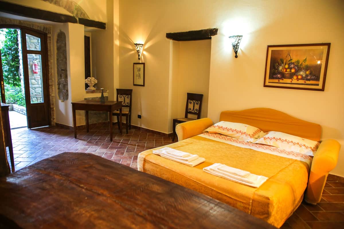 Une chambre d’hôtel avec un lit, un bureau et une chaise. Il y a un tableau au mur et une fenêtre donnant sur un paysage verdoyant.