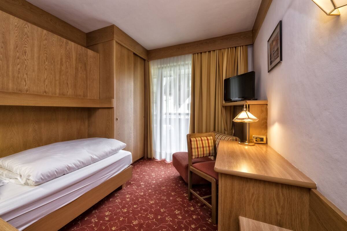 Une chambre d’hôtel avec un lit superposé, un bureau avec une lampe, une chaise, un téléviseur et une fenêtre avec des rideaux.
