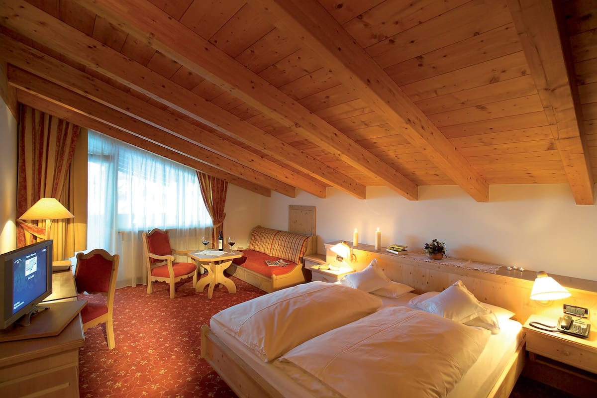 Une chambre d’hôtel avec un plafond en bois, un lit, un bureau avec un ordinateur, une chaise, une petite table et une lampe.