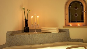 A bathroom with a freestanding bathtub, a vanity with a vase of flowers, and candles. - Hotel Armin (Selva di Val Gardena)