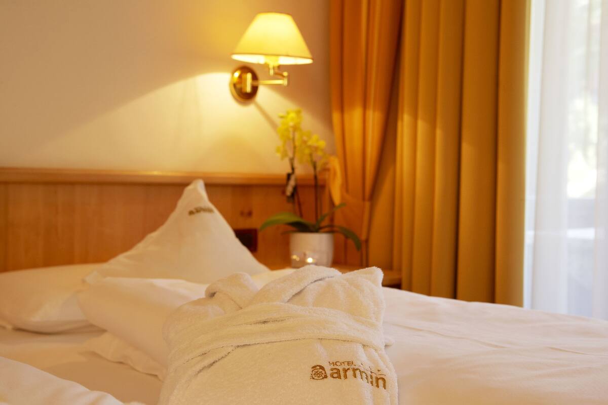 Une chambre d’hôtel avec un lit bien fait, une lampe, un vase de fleurs et une fenêtre avec des rideaux.