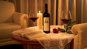 A cozy room with a table set for two, featuring a candle, a bottle of wine, and a rose. - Hotel Armin (Selva di Val Gardena)