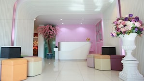 A reception area with a white reception desk, cushioned seating, and a large floral arrangement. - Pintree Service Apartment Pattaya (Pattaya)