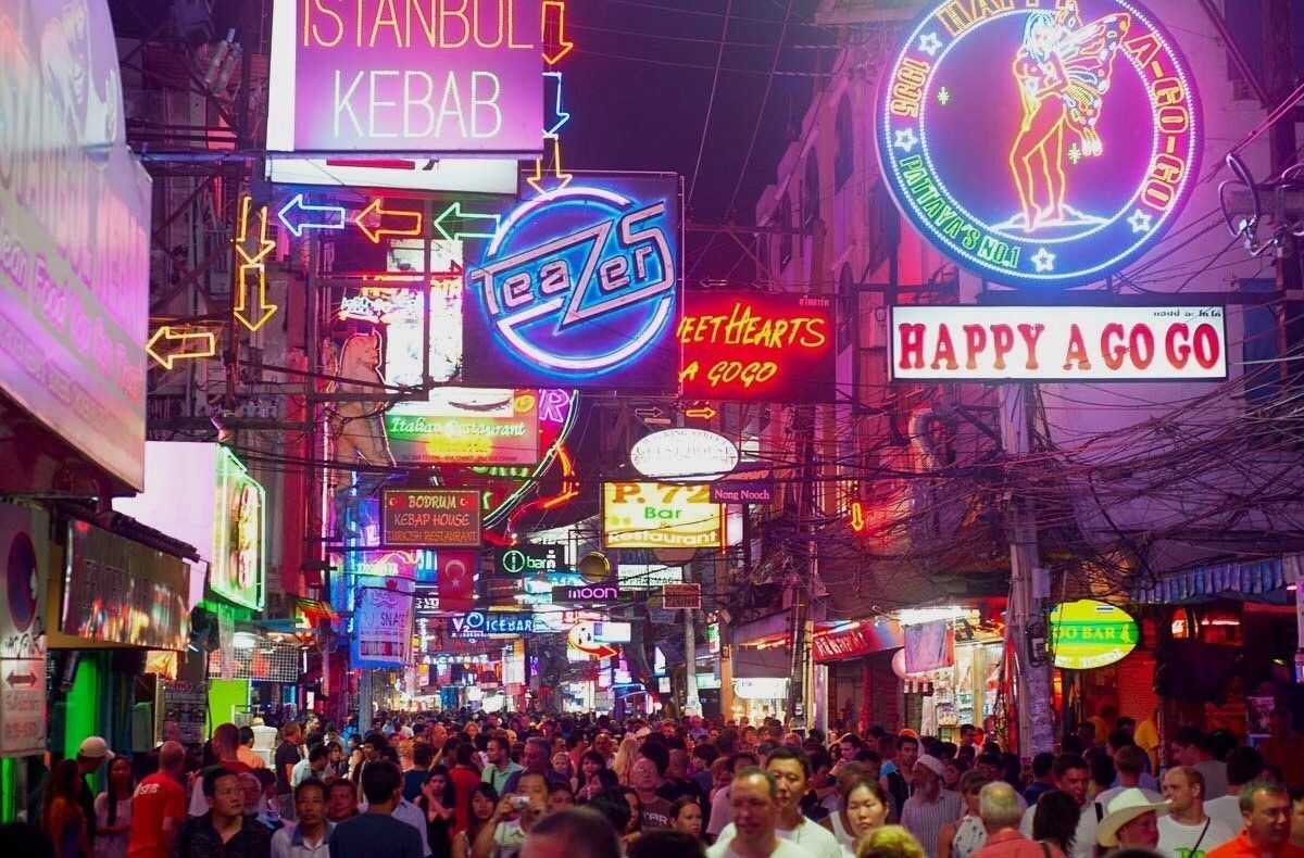 Une rue animée, bordée d’enseignes lumineuses qui font la publicité de différents commerces, notamment un restaurant de kebabs et un autre restaurant.