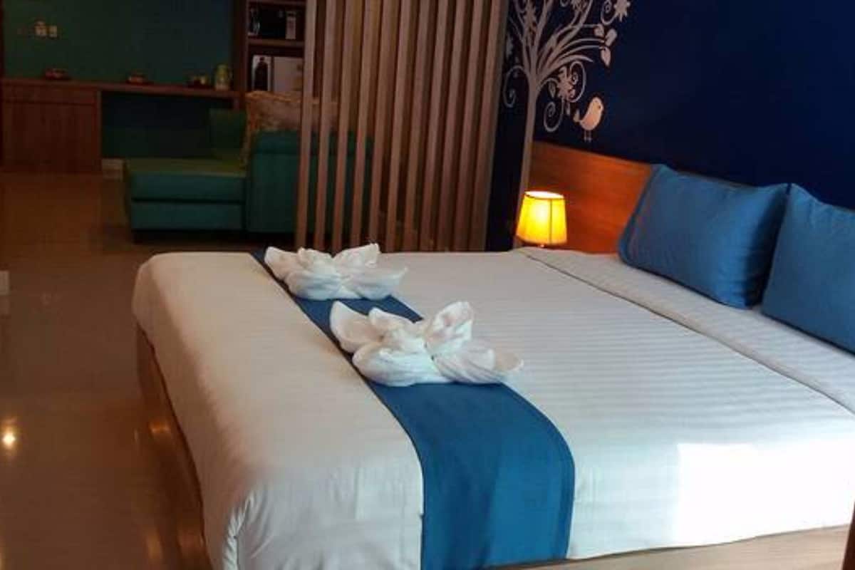 A hotel room with a large bed, a blue headboard, and a wooden floor.