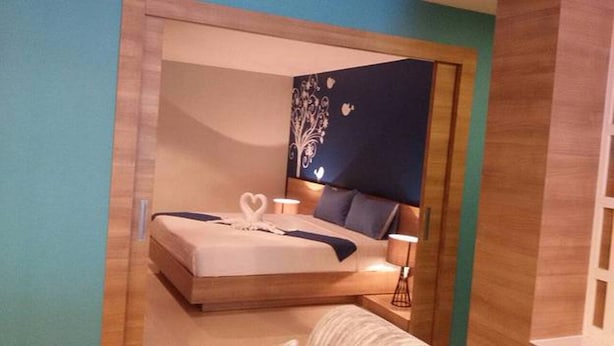 A modern bedroom with a large bed, a headboard with a decorative panel, and bedside lamps. - Pintree Service Apartment Pattaya (Pattaya)