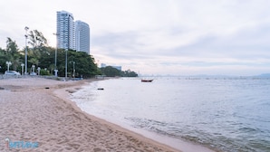 A beach with a sandy shore, a calm sea, and a row of tall buildings in the background. - Pintree Service Apartment Pattaya (Pattaya)
