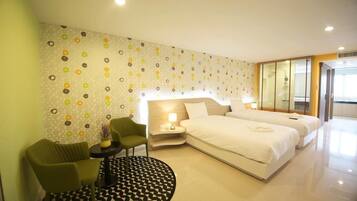 A hotel room with a large bed, two bedside tables, a green armchair, a small round table with a lamp, and a patterned wall.