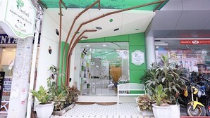 Fachada com esquema de cores verde e branco, apresentando uma entrada de vidro e plantas em vasos na frente.