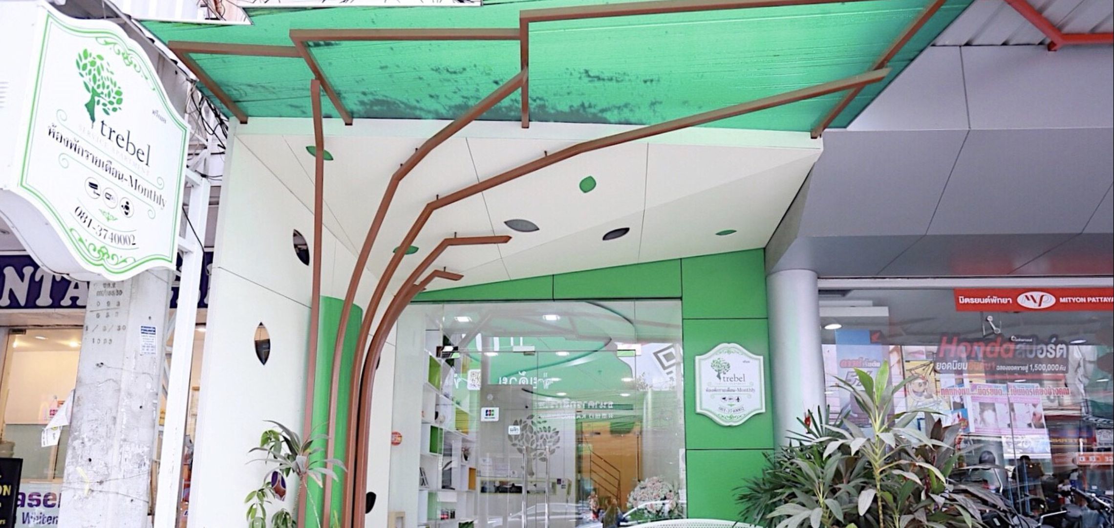 A green and white building with a modern design, featuring a glass entrance and visible interior through the windows.