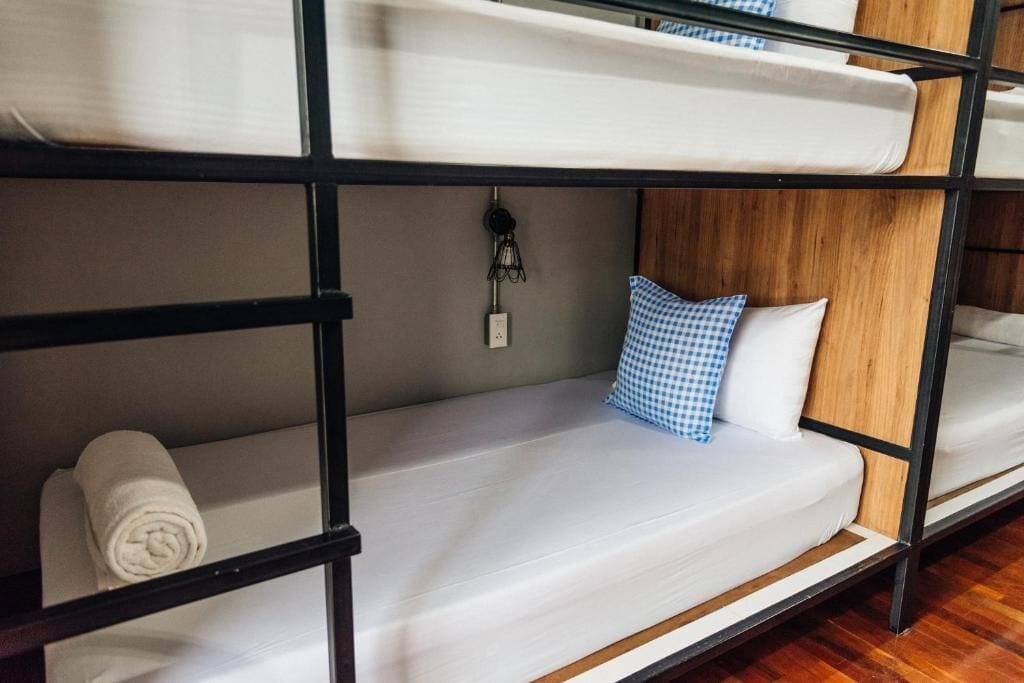 A bunk bed with a white mattress, a blue and white checkered pillow, and a rolled towel on the lower bunk.