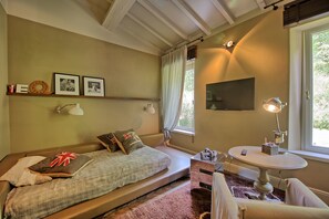 A cozy bedroom with a bed, bedside lamps, a small table, and a TV on the wall. - Villa Dora (San Gimignano)