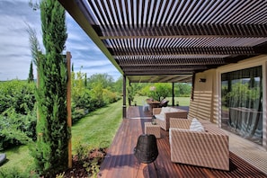 Un patio al aire libre cubierto con piso de madera, muebles de mimbre y vista a un jardín exuberante.