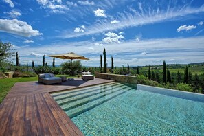 A poolside area with a wooden deck, two sofas, and an umbrella. - Villa Dora (San Gimignano)
