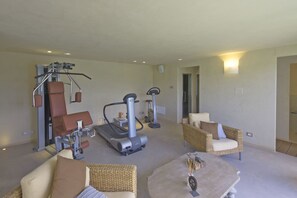 A spacious living area with exercise equipment, including a treadmill and stationary bikes, and two wicker chairs. - Villa Dora (San Gimignano)