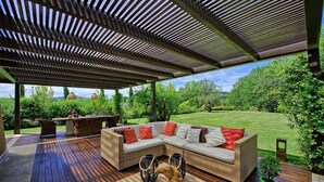 An outdoor patio with a wooden deck, a sectional sofa with cushions, wicker chairs, and a small table. - Villa Dora (San Gimignano)
