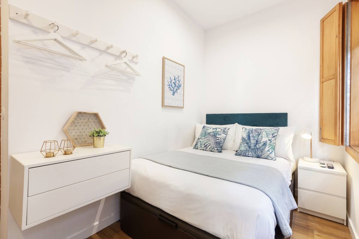 Un dormitorio ordenado con cama, mesitas de noche, cómoda y perchero en la pared.