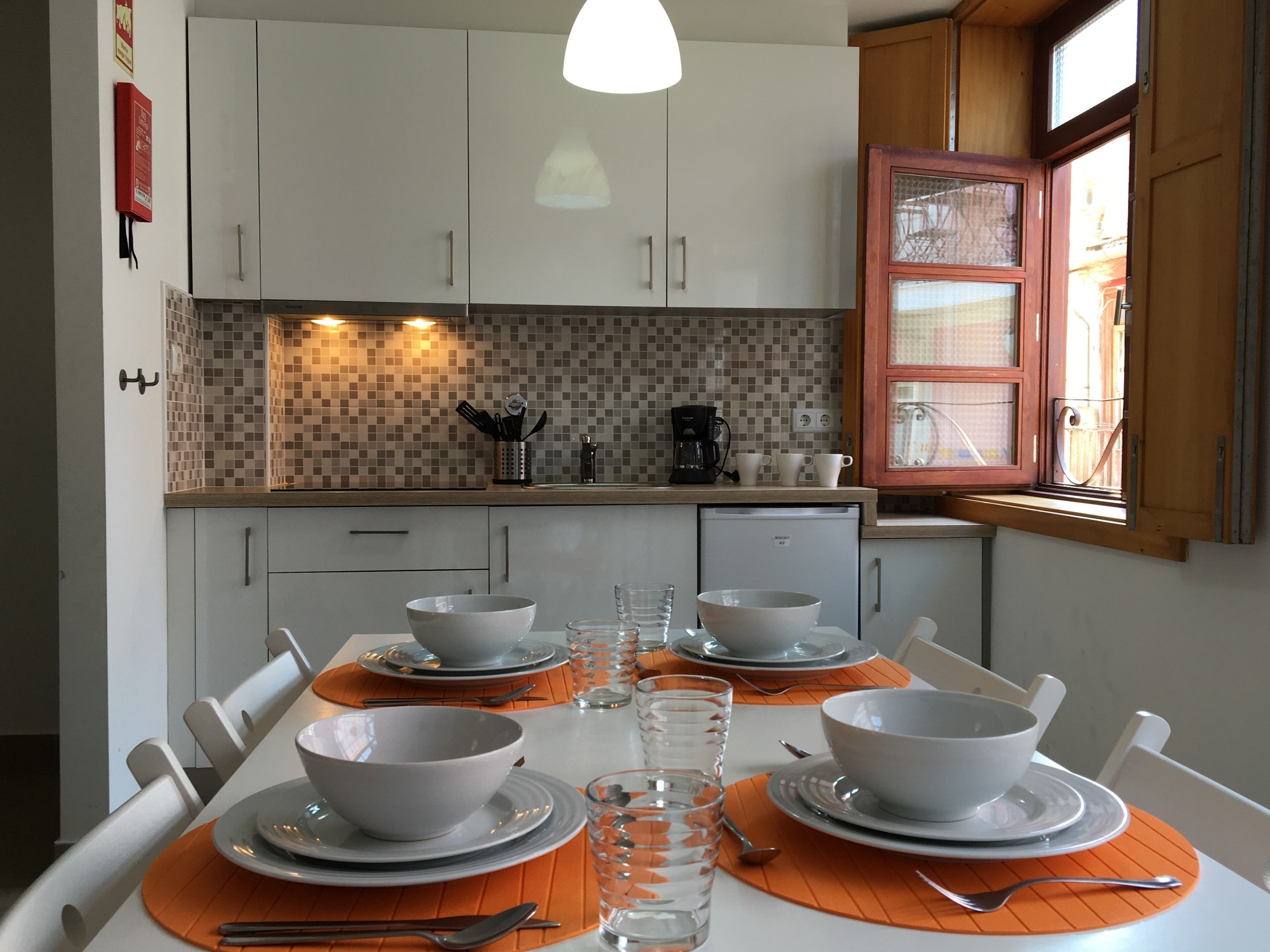 A modern kitchen with white cabinets, a tiled backsplash, and a dining table set with bowls and glasses.
