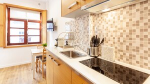 A modern kitchen with wooden cabinets, a stainless steel sink, a black induction cooktop, and a tiled backsplash. - D&S - Porto São Bento Apartments I (Porto)