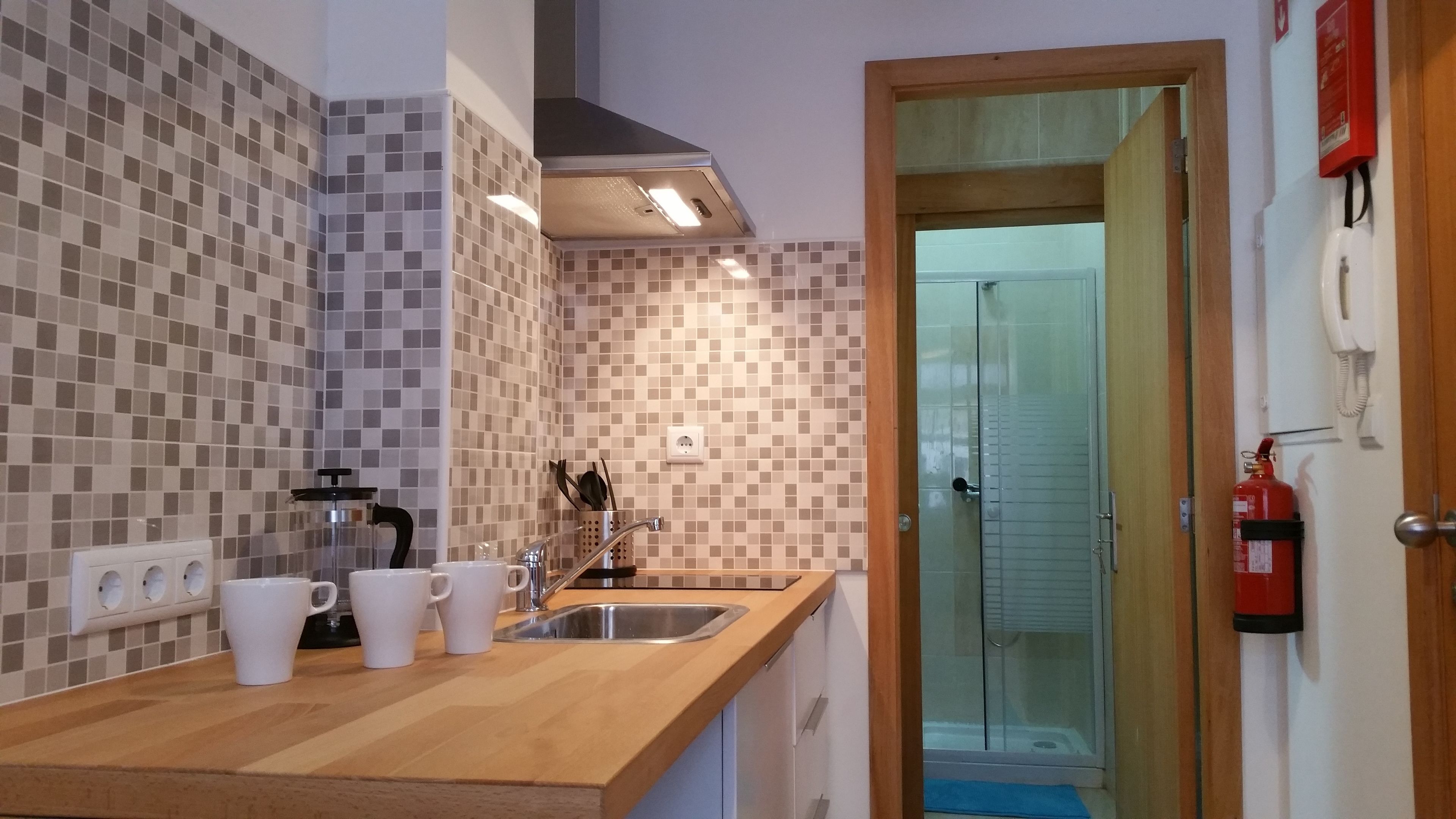 Una cucina con schienale piastrellato, macchina per il caffè, lavello e estintore.