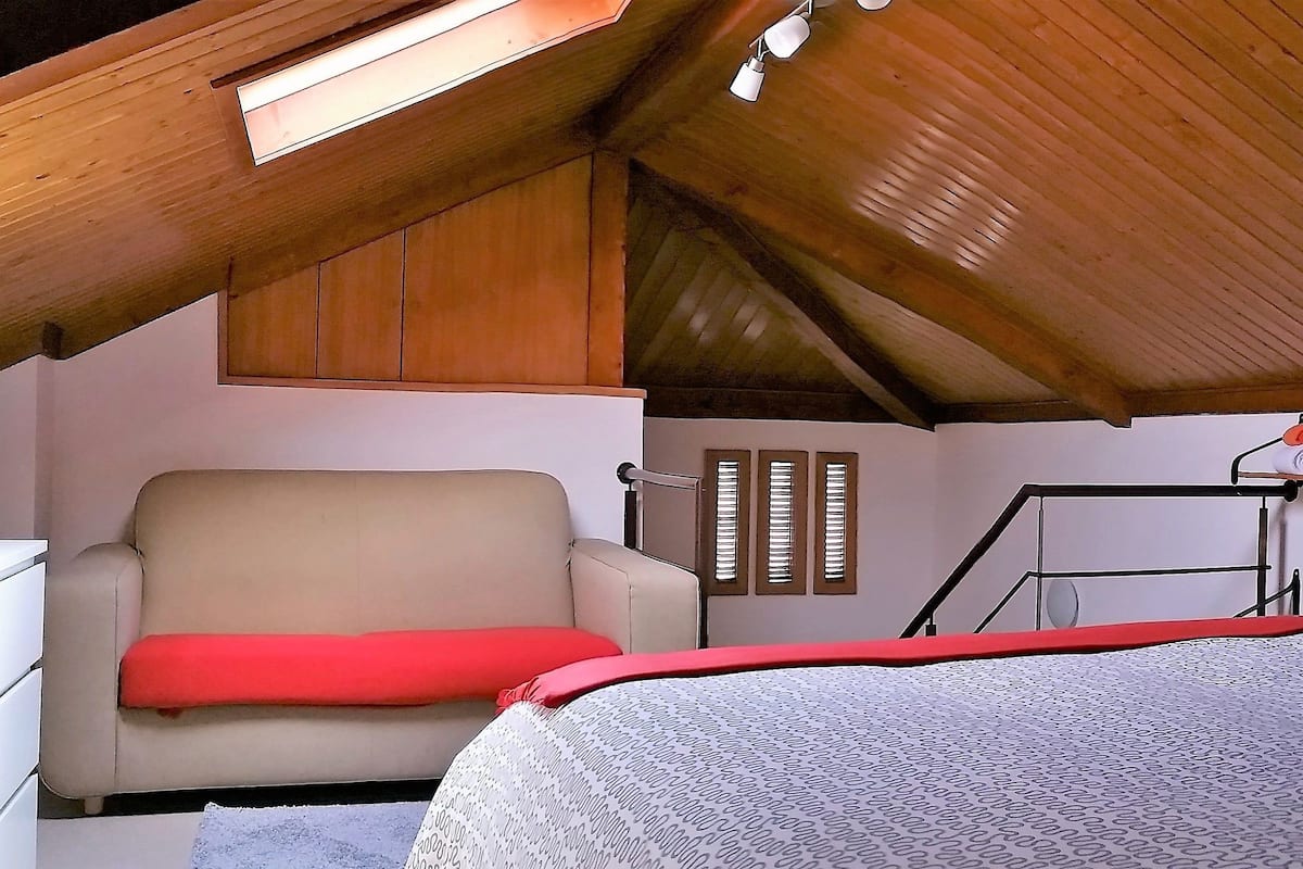 Un dormitorio con techo inclinado, una cama, una silla, un tocador y un estante con toallas.