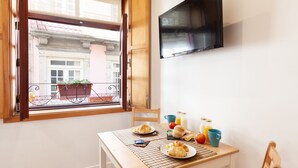 A dining area with a table set for breakfast, a TV mounted on the wall, and a view of the street outside. - D&S - Porto São Bento Apartments I (Porto)