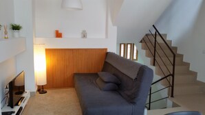 A modern living room with a grey sofa, a wooden headboard, a TV, and a staircase with a glass railing. - D&S - Porto São Bento Apartments I (Porto)