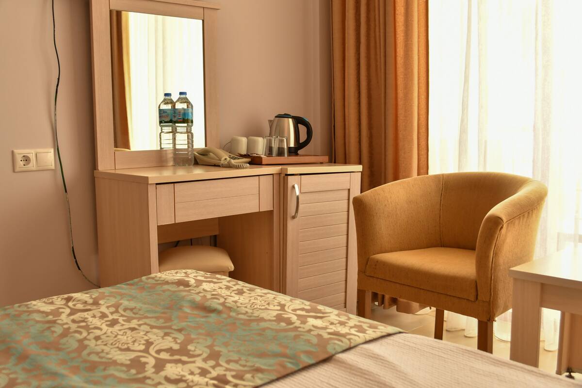 A hotel room with a bed, a desk with a telephone, a kettle, and two water bottles.