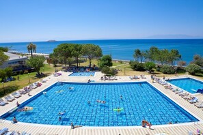 A large outdoor swimming pool with multiple lanes, surrounded by lounge chairs and umbrellas, with a view of the sea and mountains in the background. - Gumuldur Resort Hotel & SPA (Menderes)