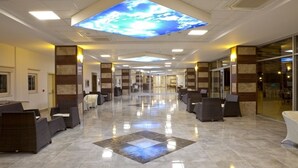 A spacious lobby with a high ceiling, a central digital display, and a tiled floor. - Gumuldur Resort Hotel & SPA (Menderes)