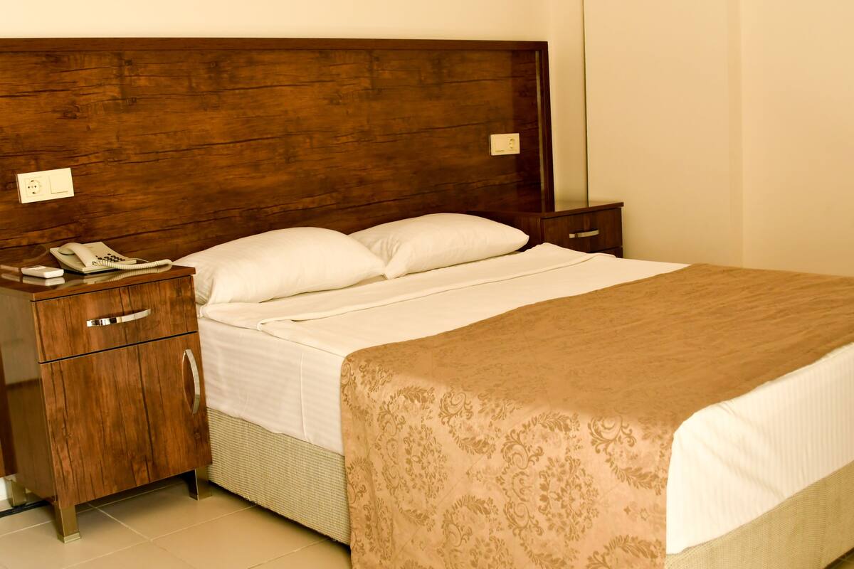 A neatly made bed with a wooden headboard, a bedside table with a phone, and a drawer unit.